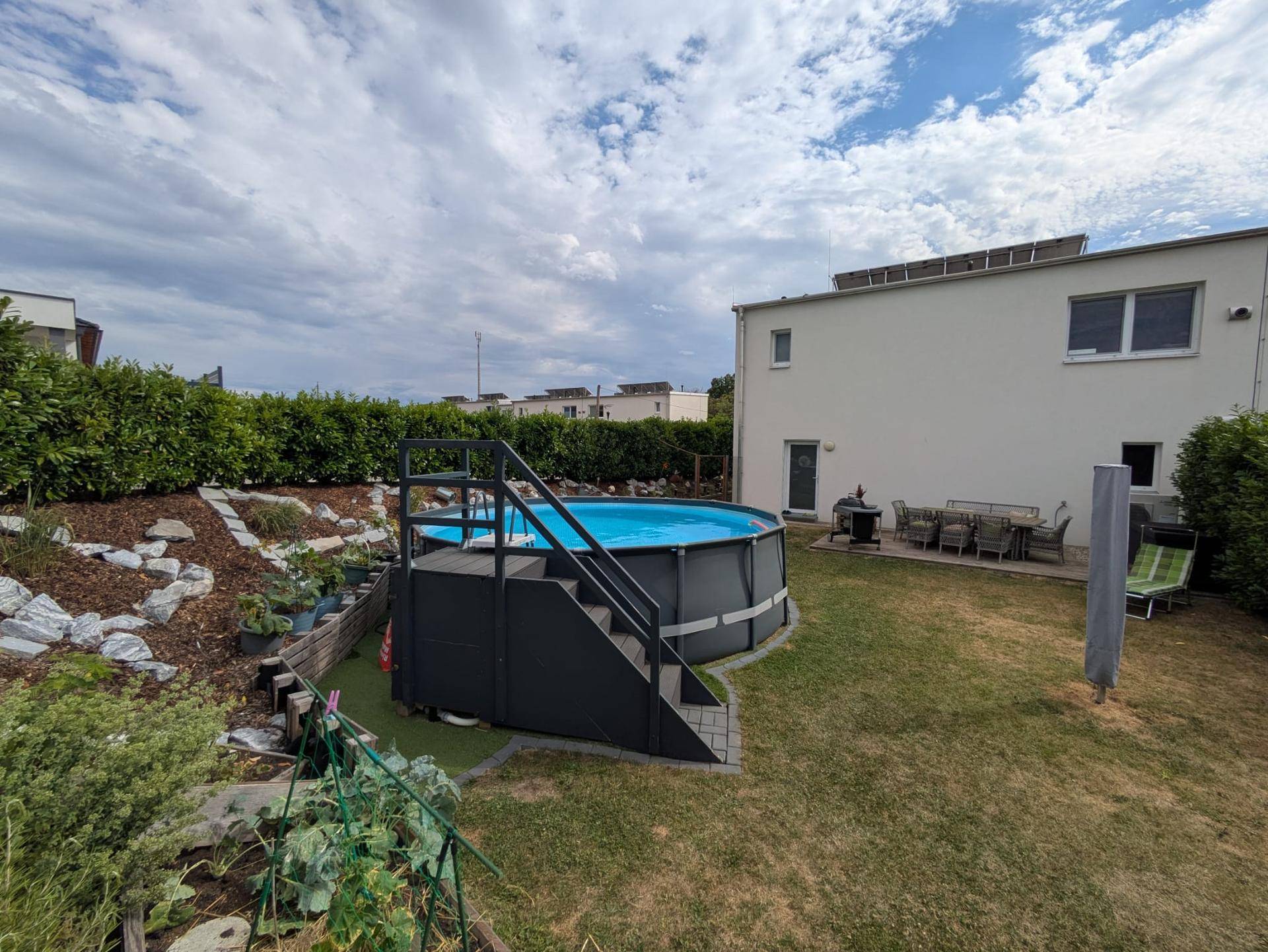 Garten mit großem Aufstellpool, Liegewiese und terrassierten Beeten.