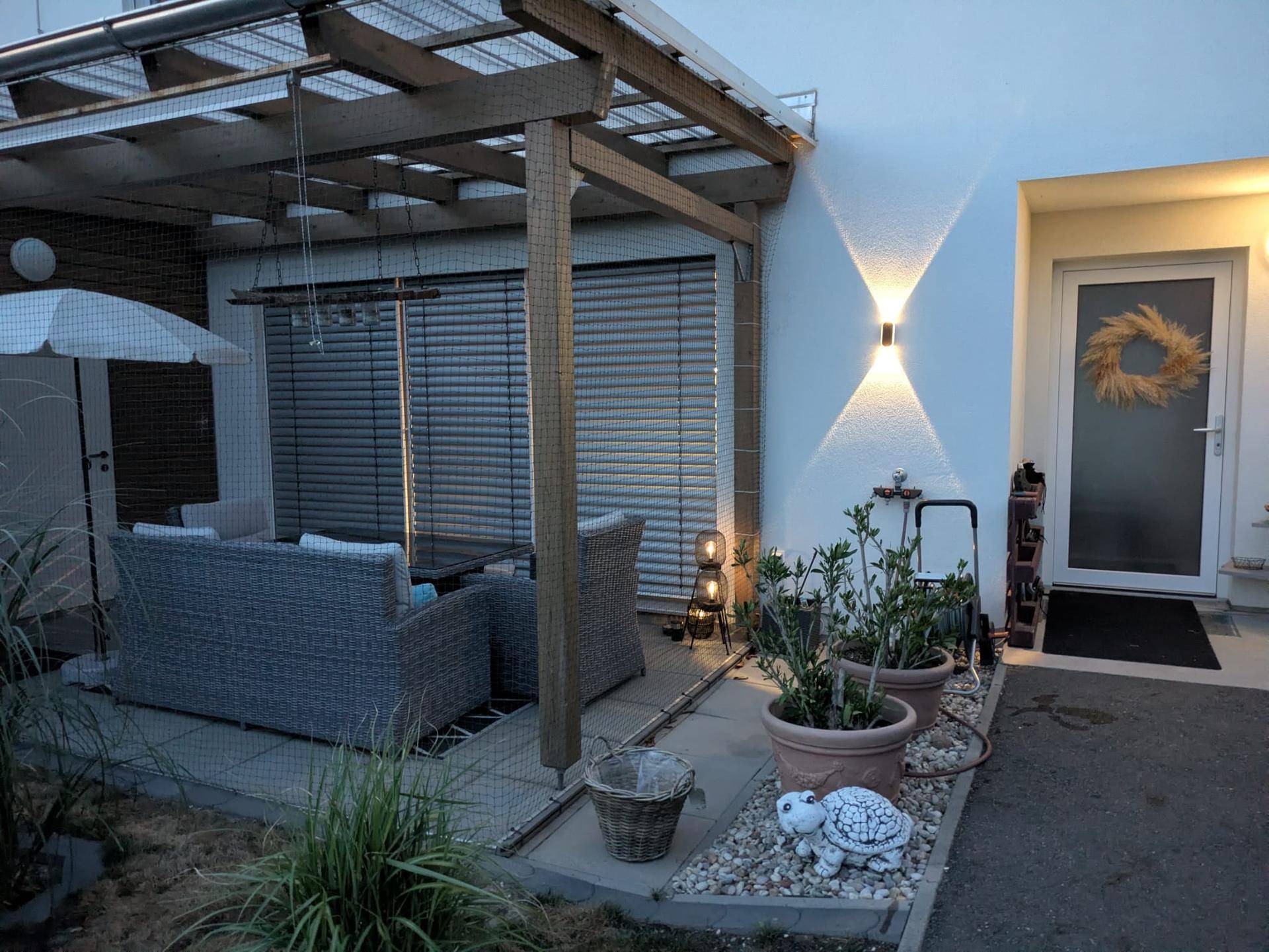 Überdachte Terrasse am Abend mit gemütlichen Rattanmöbeln und Pflanzen.