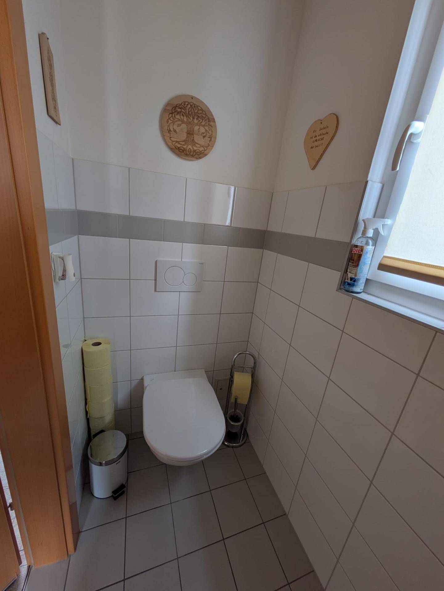 Gäste-WC mit Wand-WC, Fliesenboden und einem kleinen Fenster.