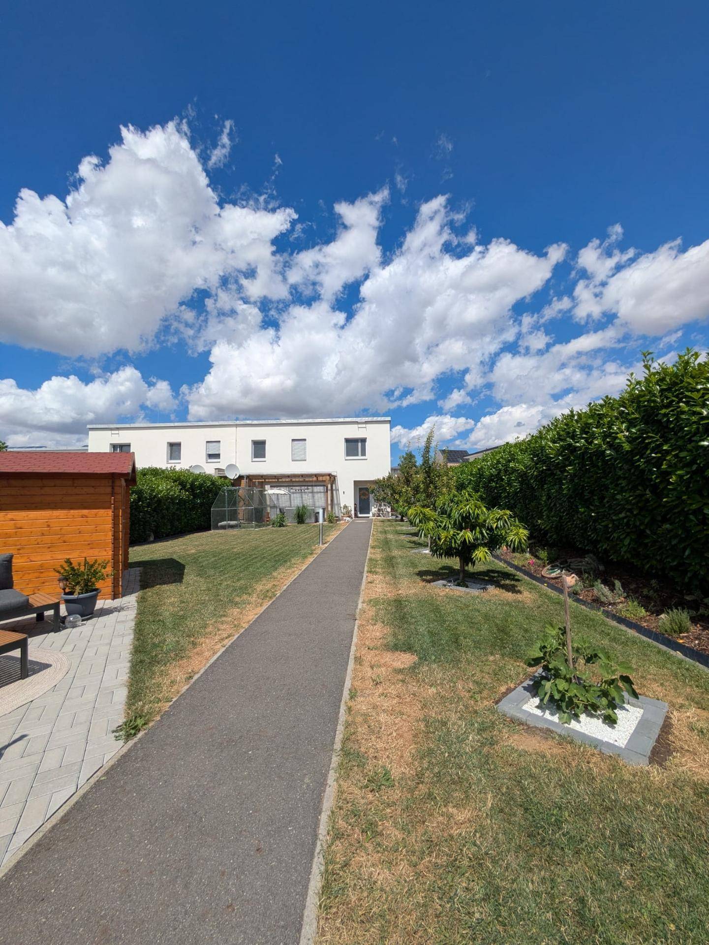 Gepflegter Garten mit Rasenfläche, Gartenweg und Blick auf das moderne Wohnhaus.