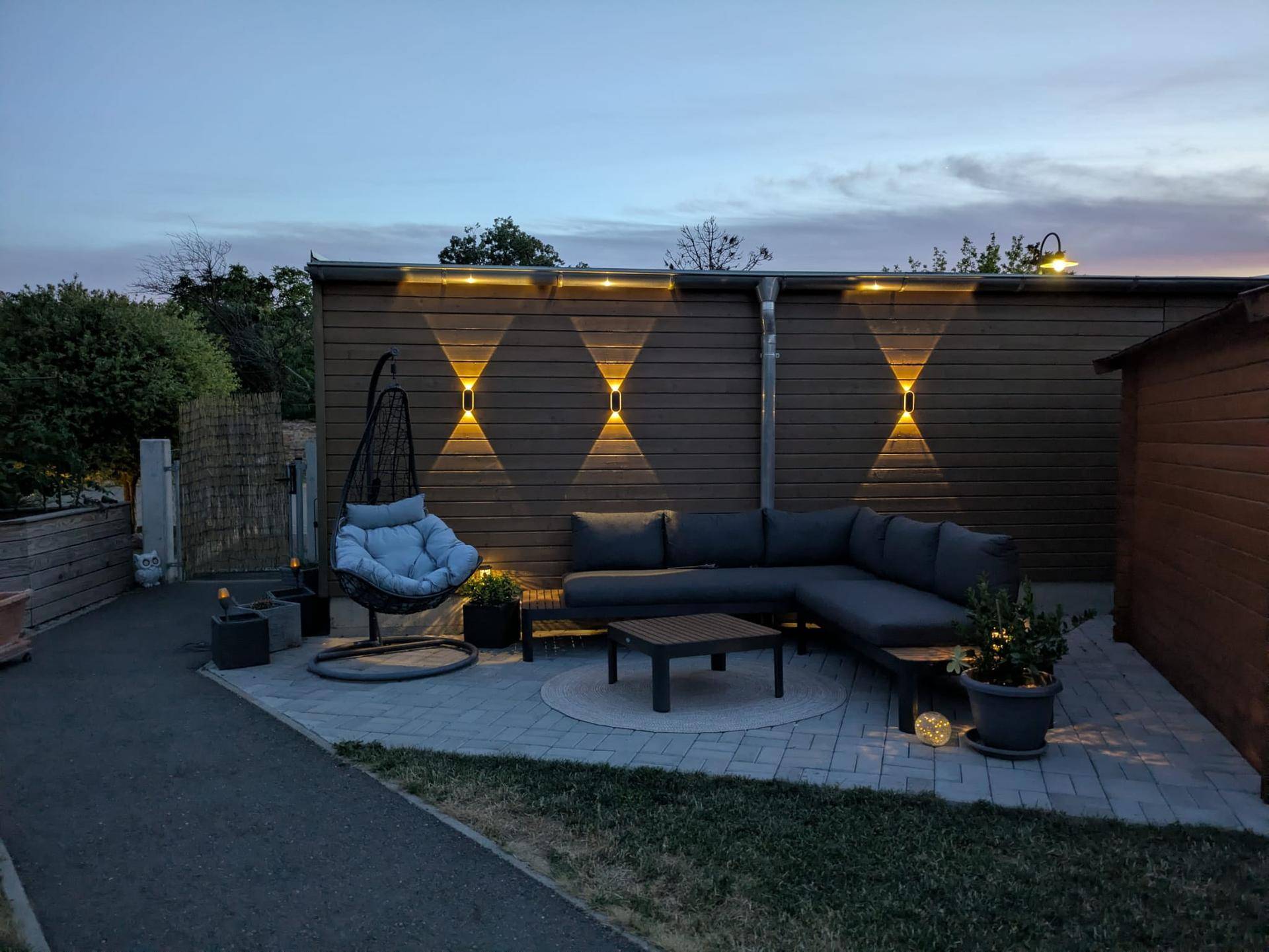 Gemütliche Terrasse am Abend mit Lounge-Möbeln und stimmungsvoller Wandbeleuchtung.