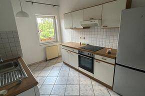 Funktionale Küche mit weißen Schränken, Holzarbeitsplatten, Einbaugeräten und Fliesenboden.