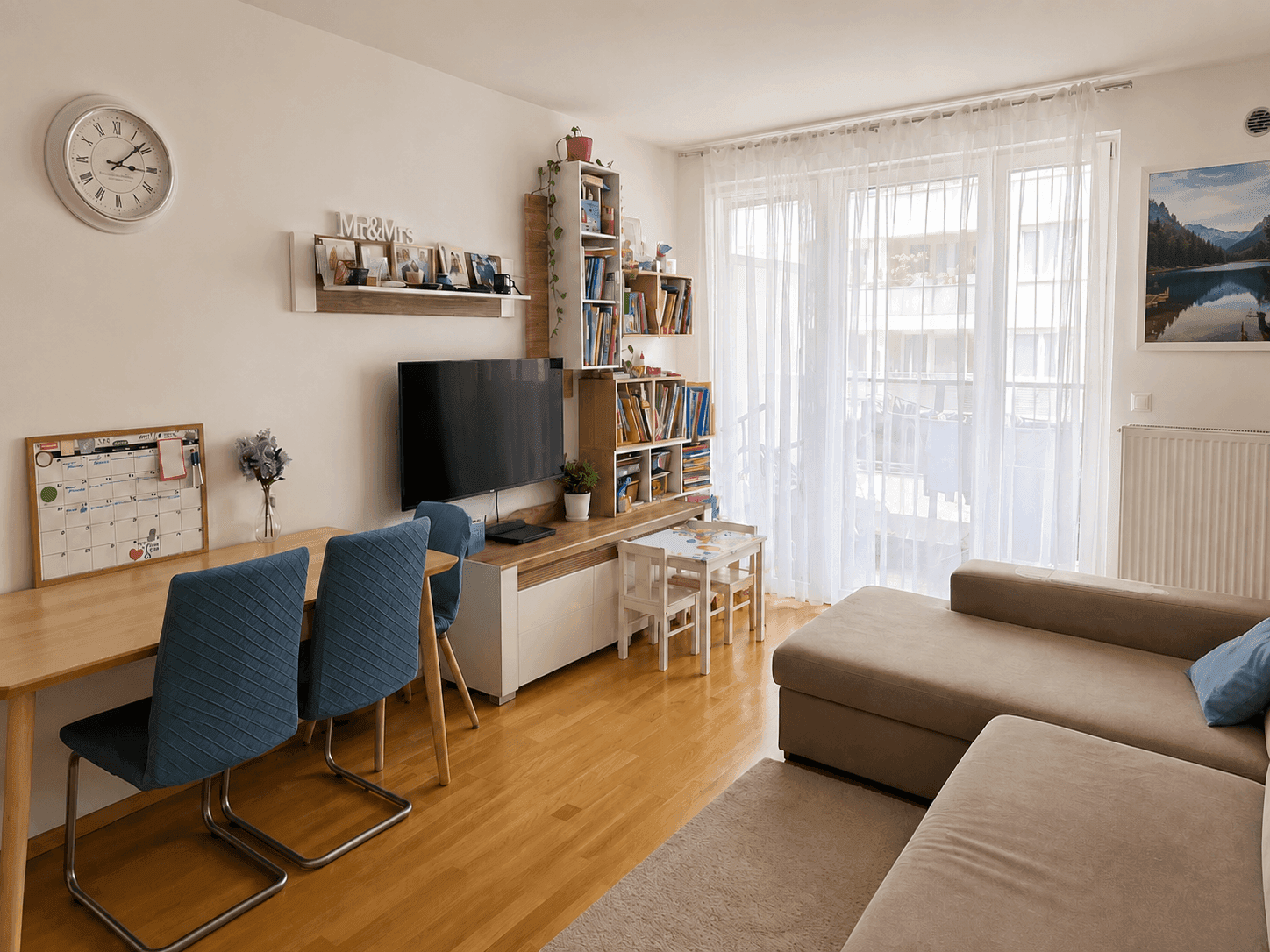 Helles Wohnzimmer mit Holzboden, großem Sofa und Zugang zu einem Balkon.
