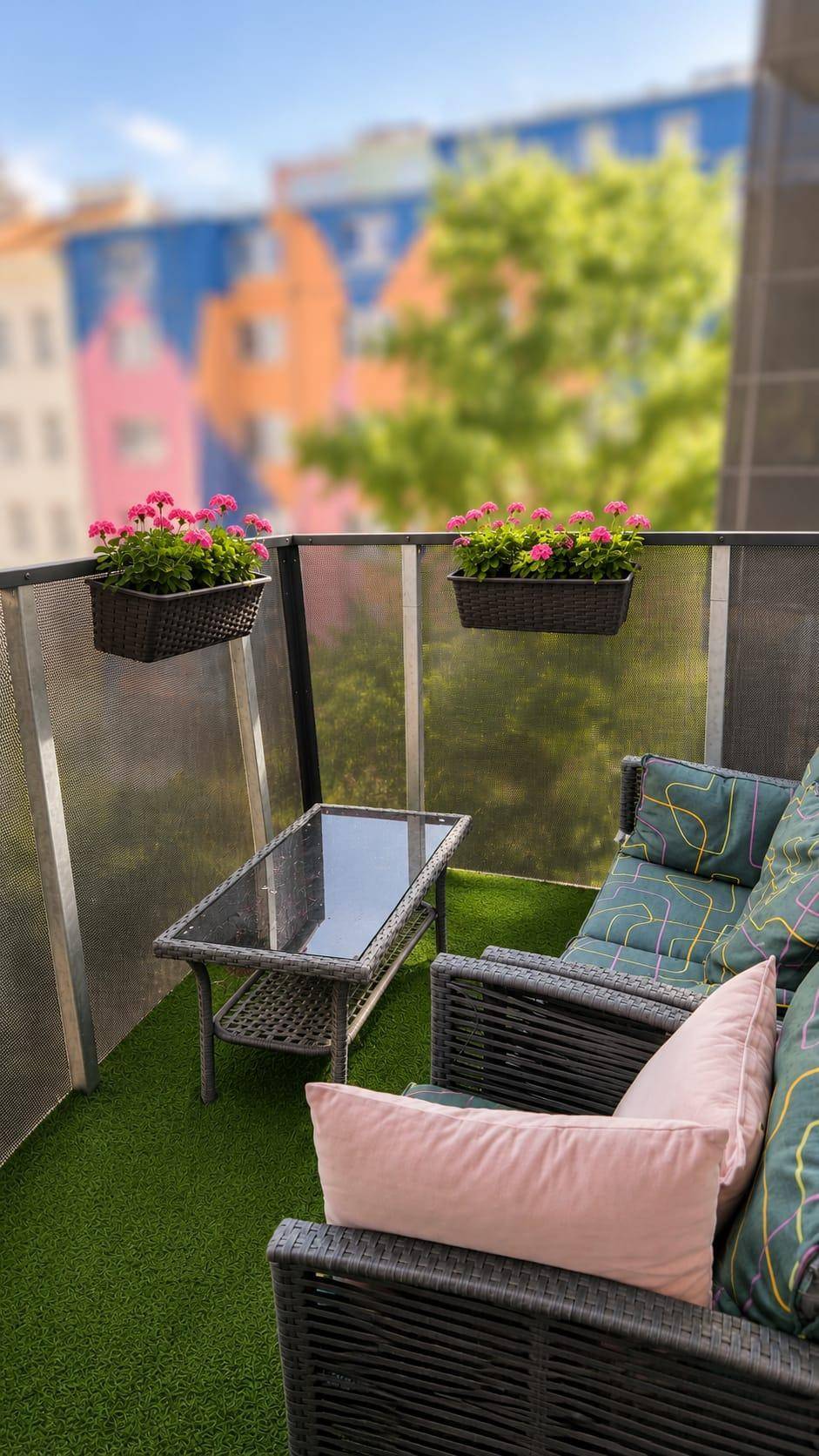 Gemütlicher Balkon mit Kunstrasen, Sitzgelegenheiten und bunten Blumenkästen.