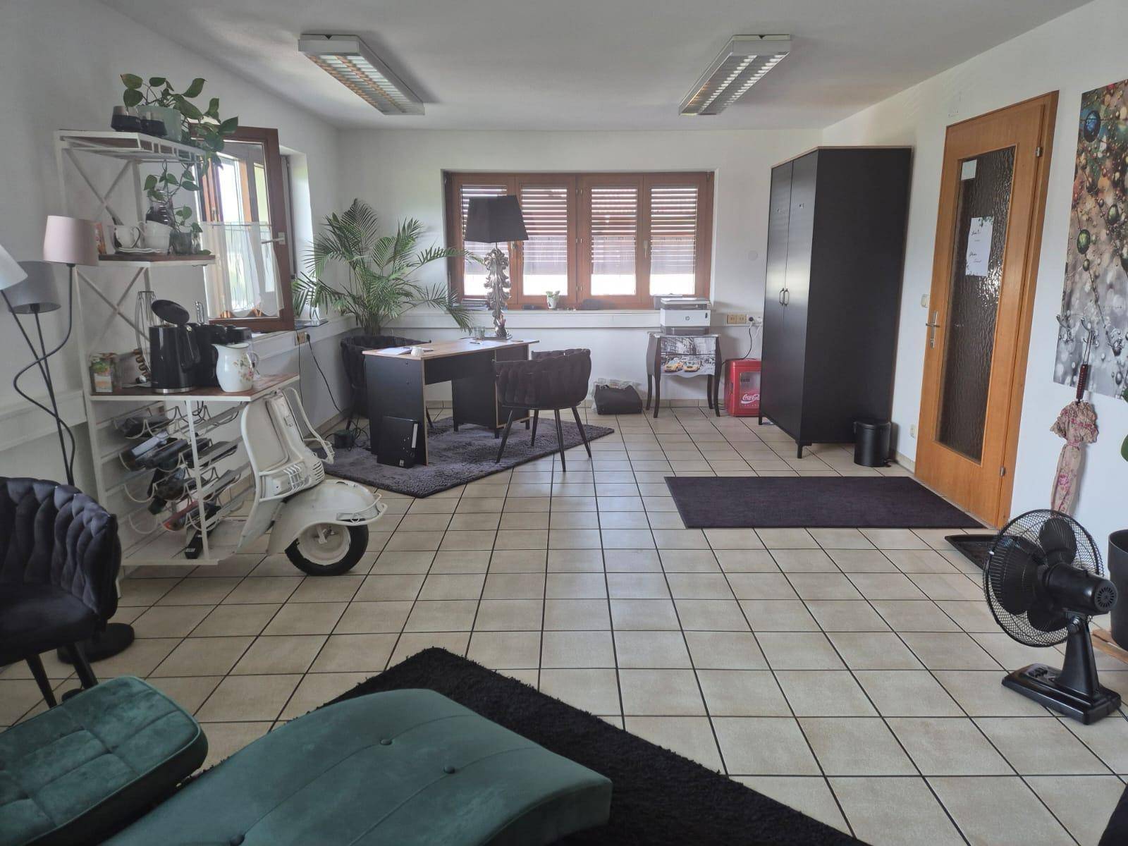Arbeitsbereich mit Schreibtisch, dunklem Schrank und einem dekorativen Roller als Regal, beleuchtet durch ein großes Fenster.