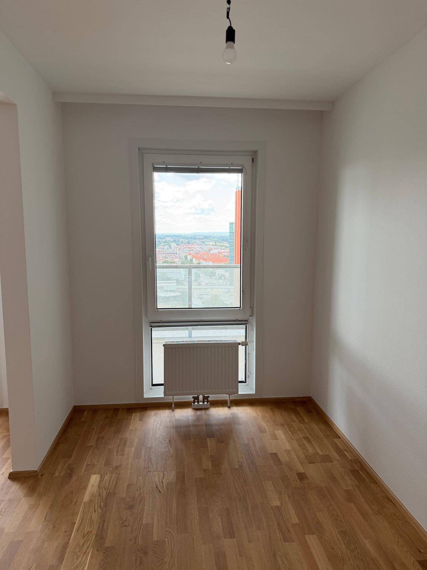 Heller Raum mit Eichenparkettboden und einem großen Fenster, das einen weiten Blick bietet.