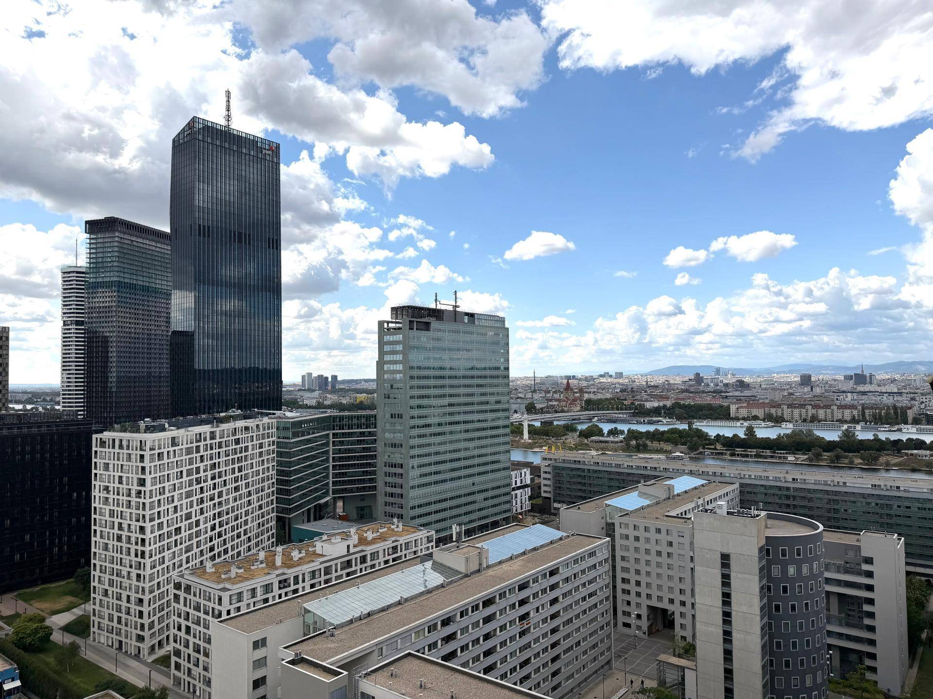 Panoramablick auf die moderne Stadtlandschaft mit Hochhäusern und dem Fluss im Hintergrund unter blauem Himmel.