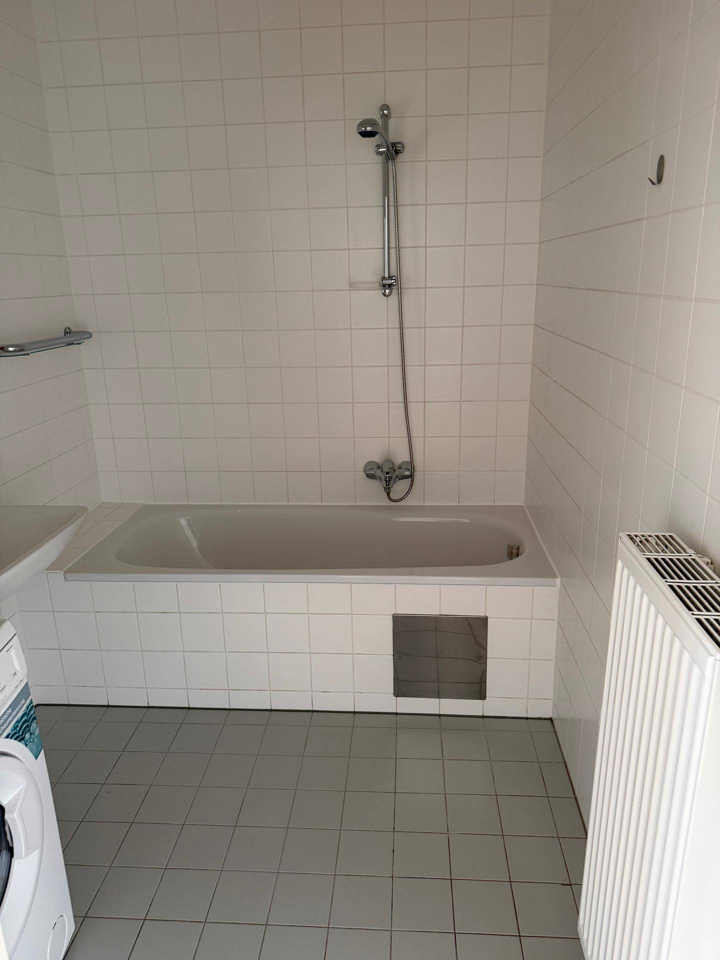 Helles Badezimmer mit weiß gefliester Badewanne und Duschvorrichtung, sauber und funktional.