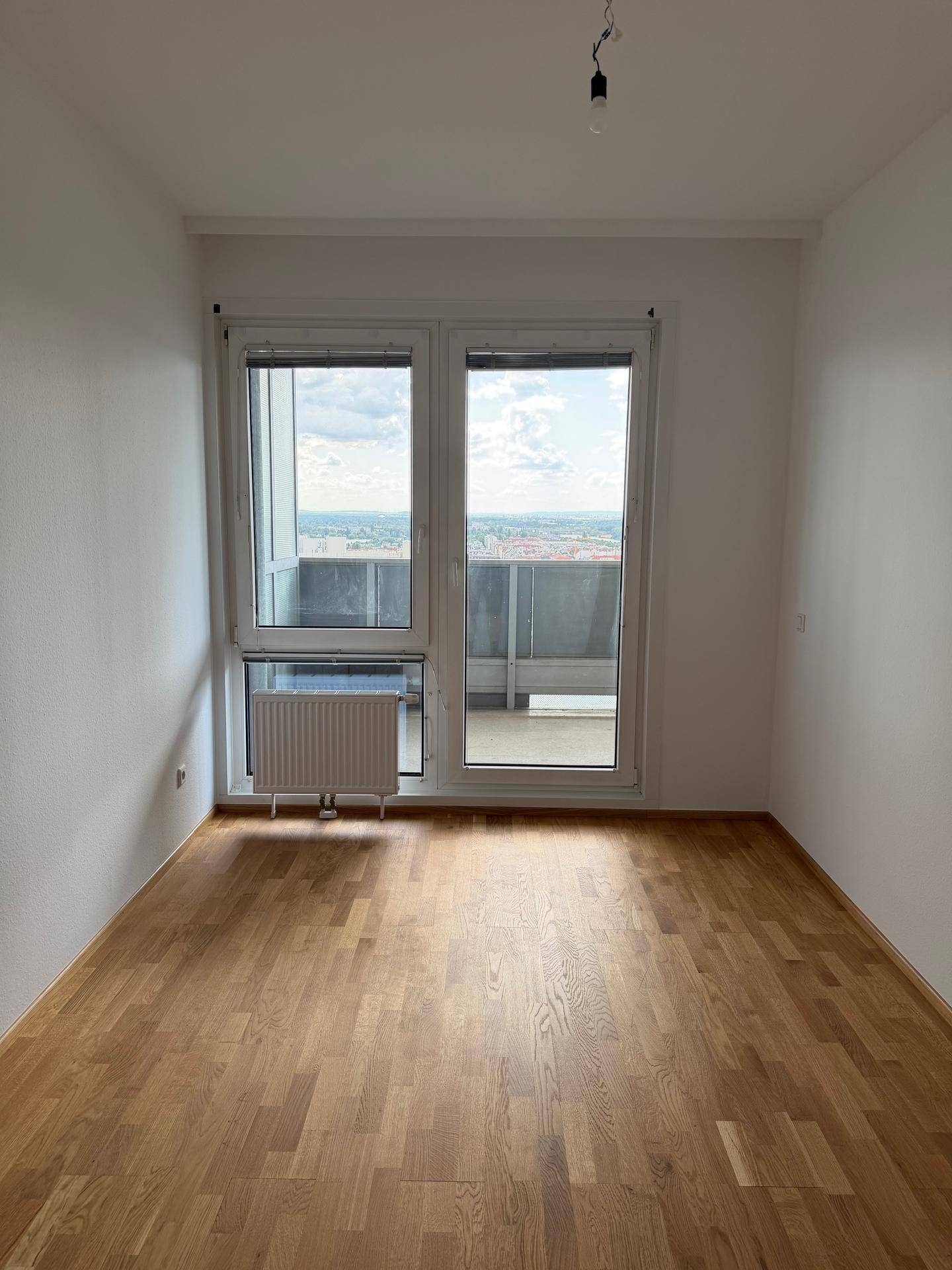 Helles Schlafzimmer mit Eichenparkettboden und großem Fenster, das viel Tageslicht hereinlässt.
