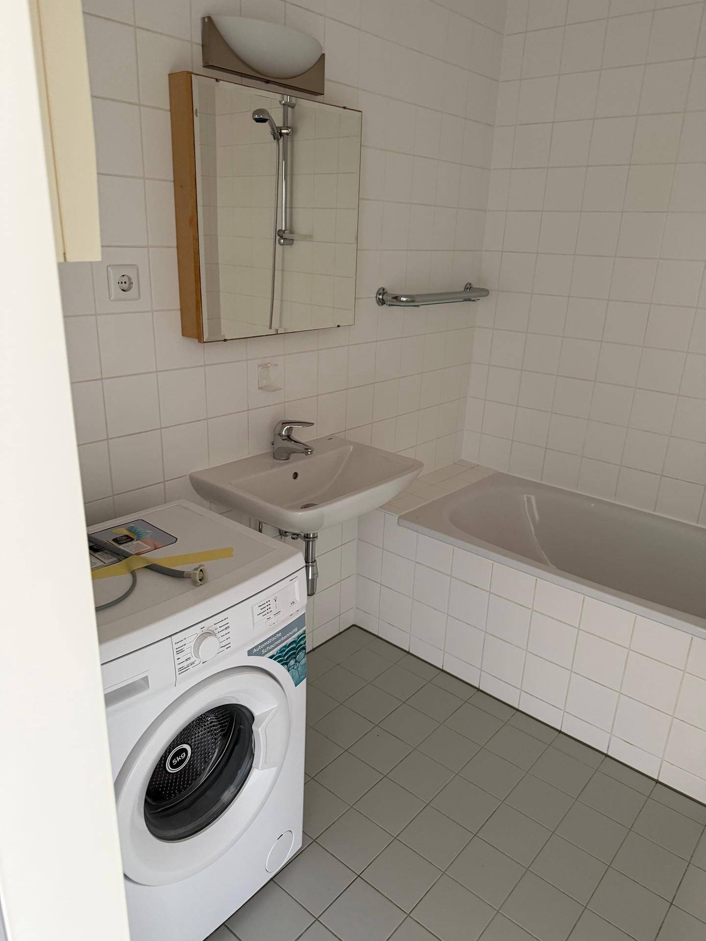 Gefliestes Badezimmer mit Badewanne, Waschbecken und einer Waschmaschine, in gutem Zustand.