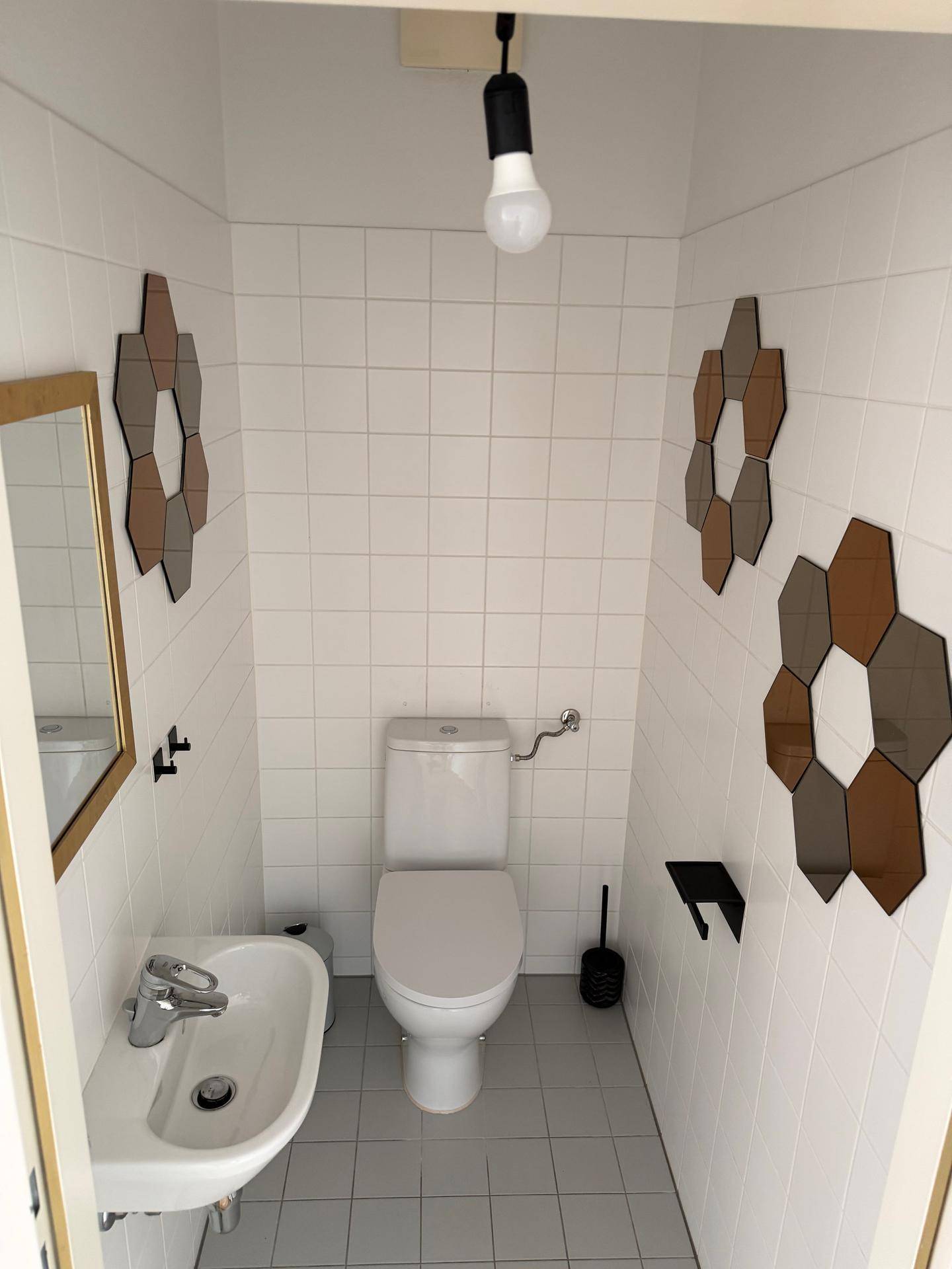 Modernes Gäste-WC mit weißer Toilette, kleinem Waschbecken und dekorativen Spiegelelementen.