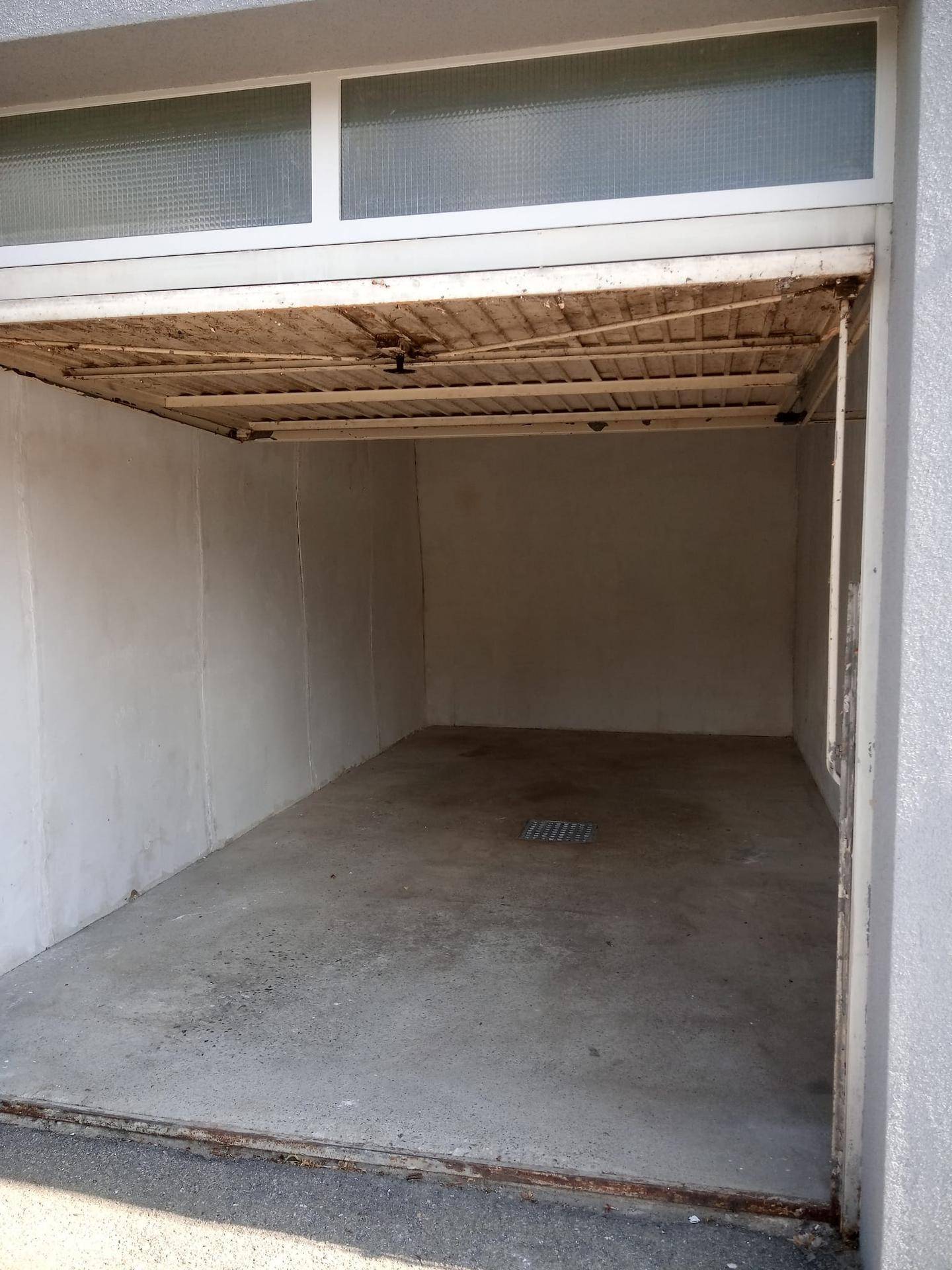 Blick in eine leere Garage mit offenem Tor und Oberlichtfenster.