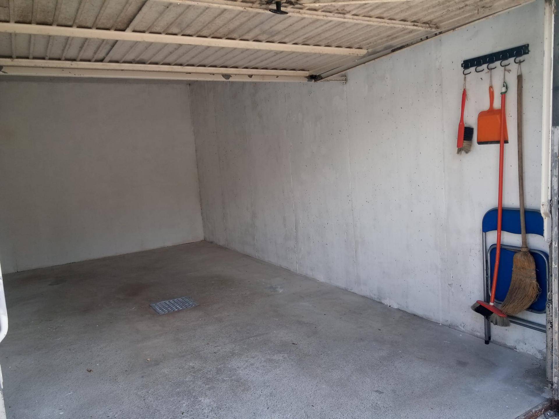Leere Garage mit Betonboden und Wänden, ausgestattet mit Reinigungsutensilien.