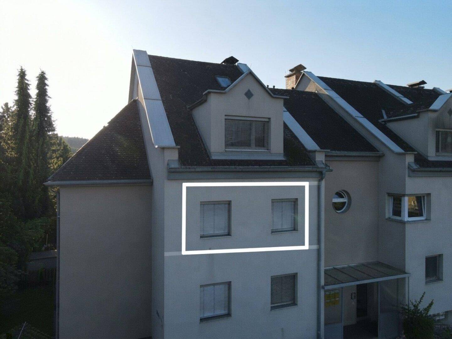 Fassade des Mehrfamilienhauses mit Fenstern und Dachgauben unter klarem Himmel.