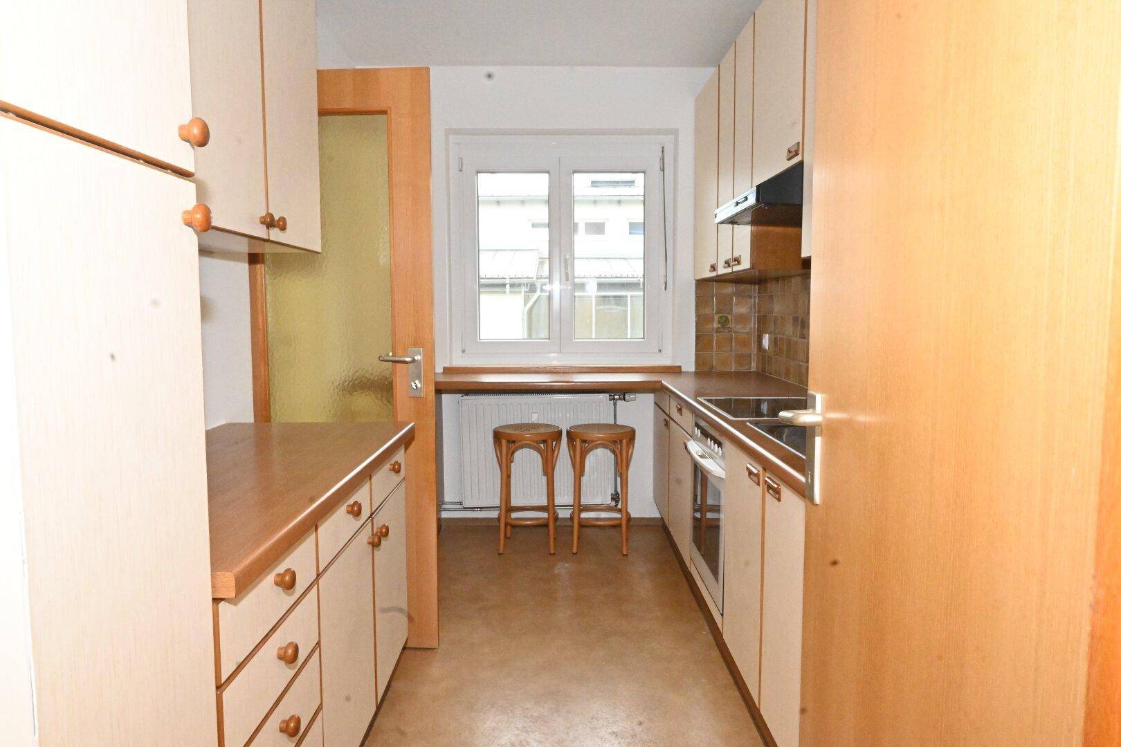 Funktionale Küche mit hellen Holzschränken, Arbeitsplatten und Fensterblick.