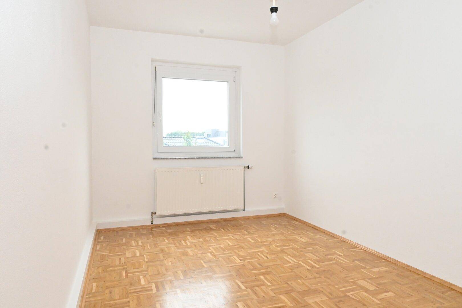 Ruhiges Schlafzimmer mit Parkettboden und Fenster, das viel Tageslicht spendet.