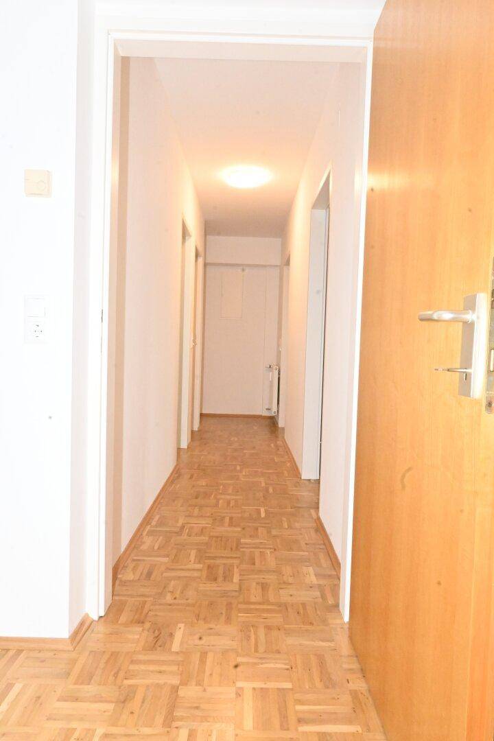 Langer Flur mit Parkettboden, der zu weiteren Zimmern der Wohnung führt.
