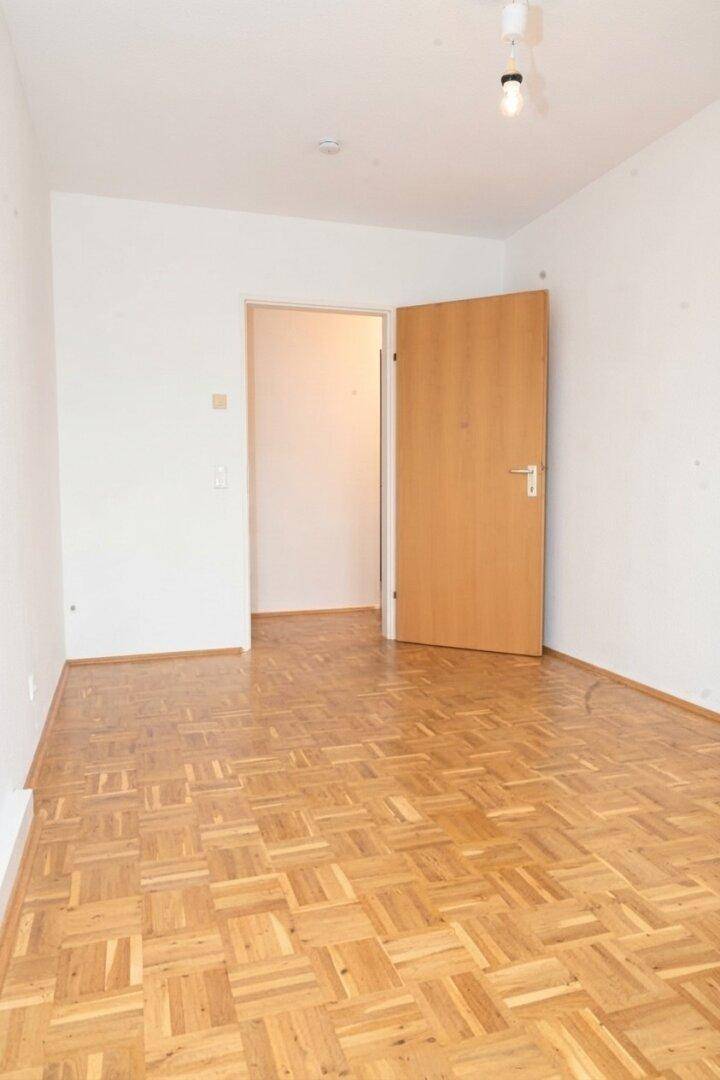 Geräumiges Schlafzimmer mit Parkettboden und Holztür zu einem angrenzenden Raum.