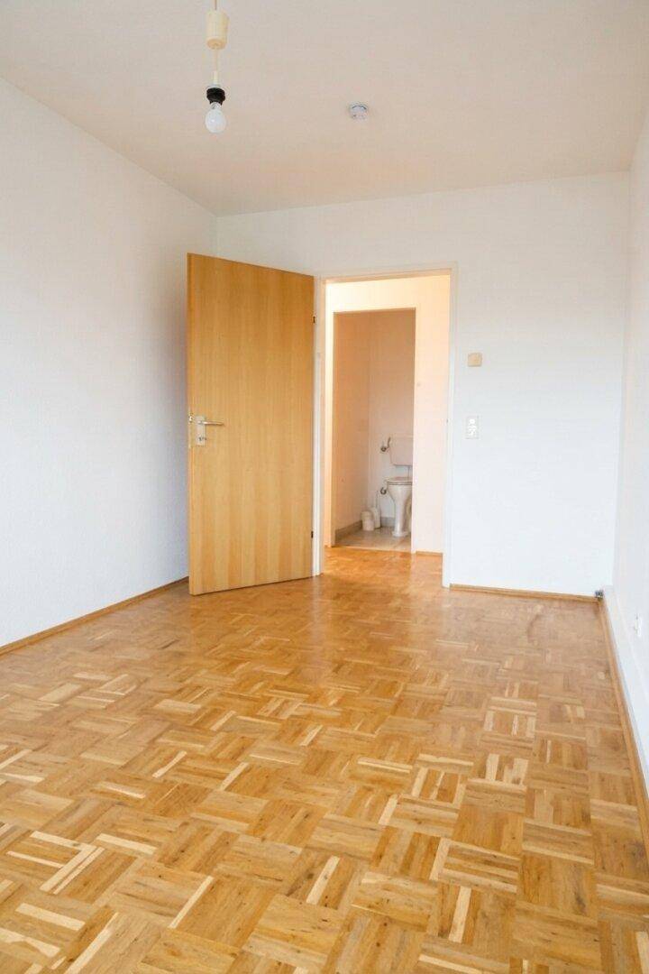 Schlafzimmer mit Parkettboden und Zugang zu einem separaten WC-Bereich.