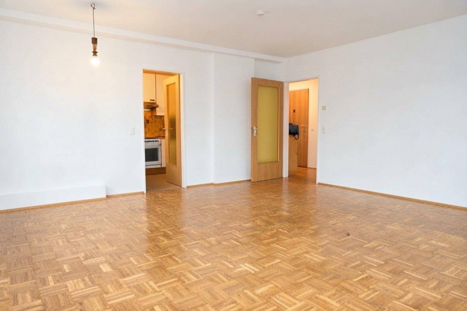 Geräumiges Wohnzimmer mit Parkettboden und Türen zu angrenzenden Räumen.