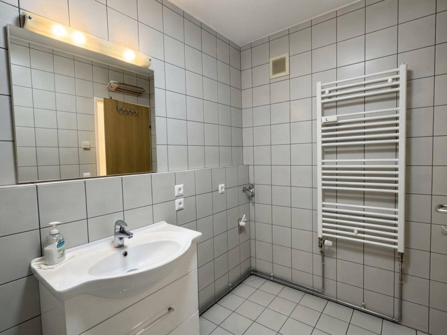 Badezimmer mit Fliesenboden, Waschbecken, Spiegel und beheiztem Handtuchhalter.