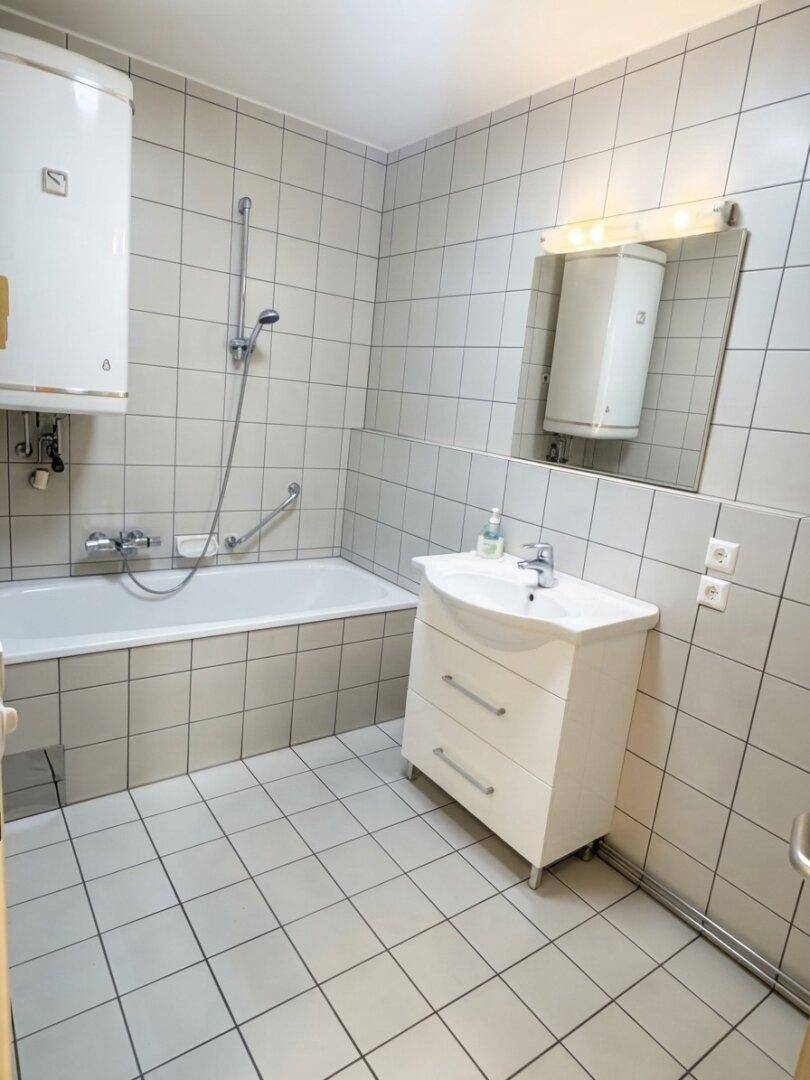 Gefliestes Badezimmer mit Badewanne, Waschbecken und Warmwasserboiler.