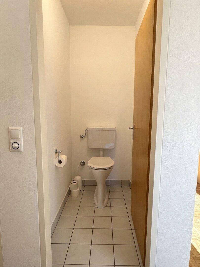 Separates WC mit Fliesenboden und Standard-Toilette in schlichtem Design.