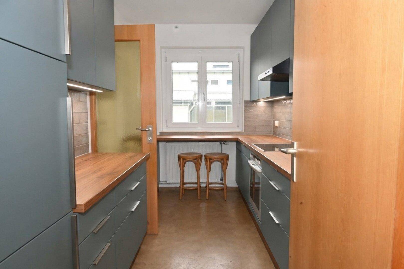 Moderne Küche mit grauen Schränken, Holz-Arbeitsplatten und Fenster über der Spüle.