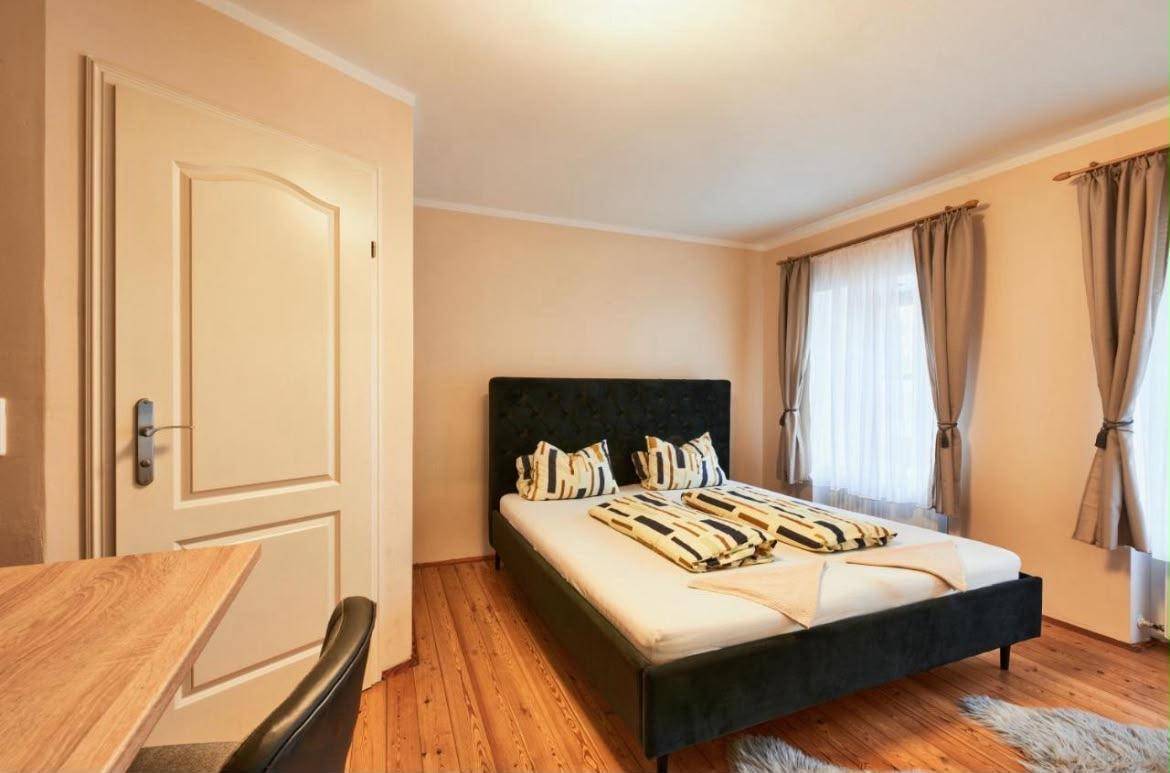 Schlafzimmer mit Doppelbett, Holzboden und einem Schreibtischbereich am Fenster.
