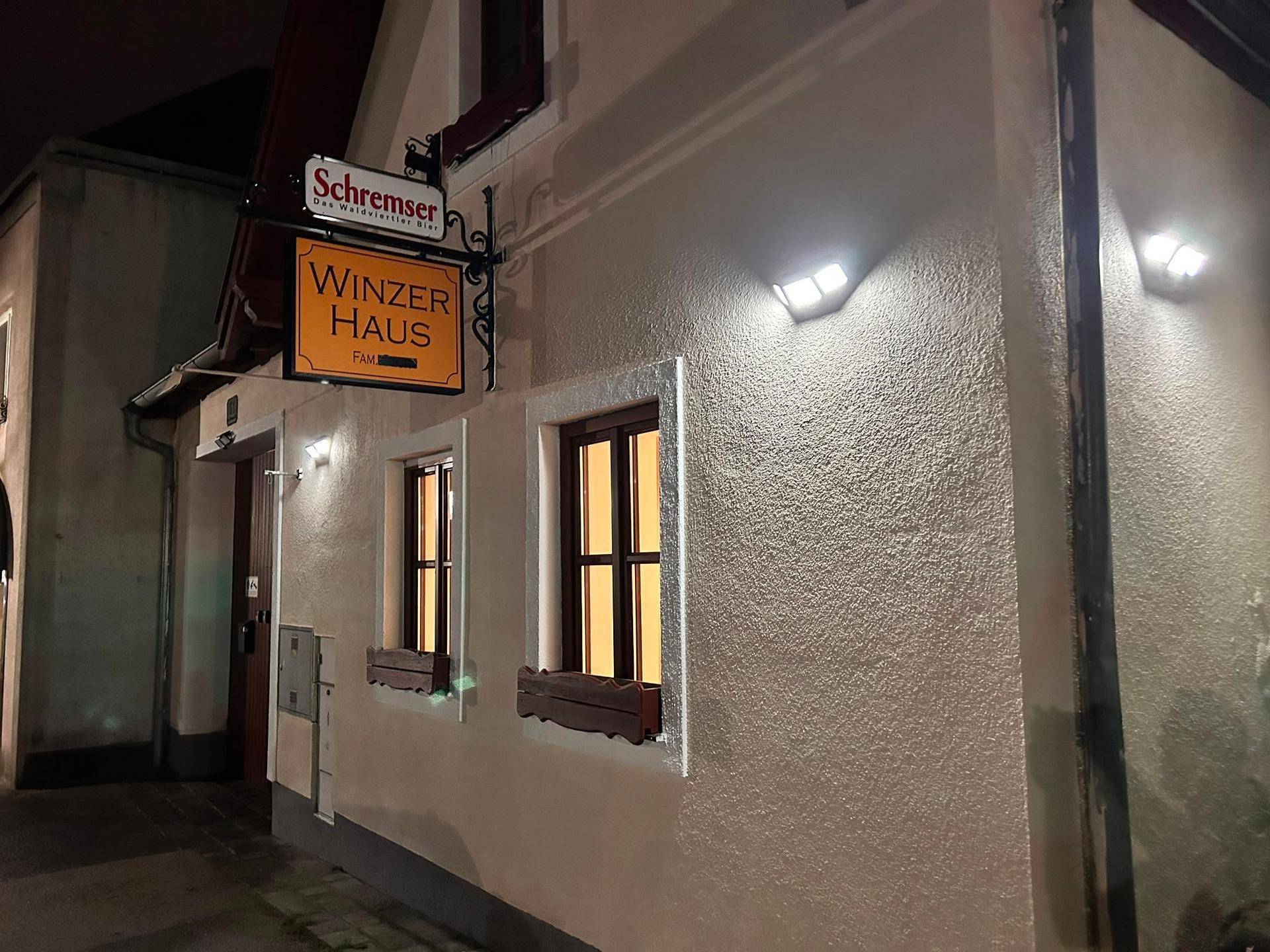 Nahaufnahme der beleuchteten Fassade eines Winzerhauses mit Fenstern und traditioneller Beschilderung.