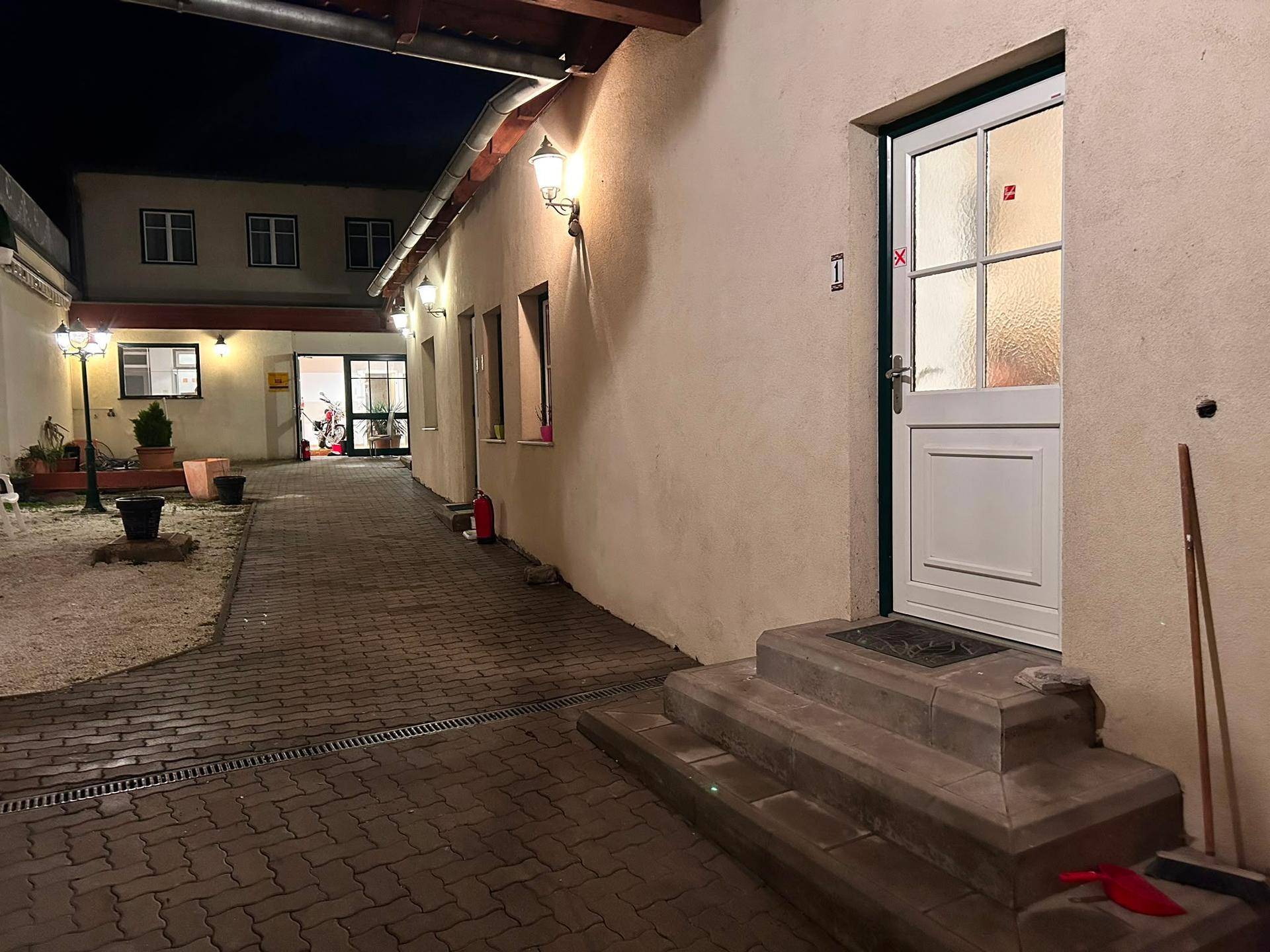 Gepflasterter Innenhof mit Beleuchtung und Zugang zu verschiedenen Gebäudeteilen bei Nacht.
