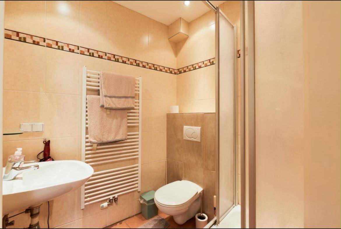Modernes Badezimmer mit Dusche, WC und beheiztem Handtuchhalter auf beigefarbenen Fliesen.
