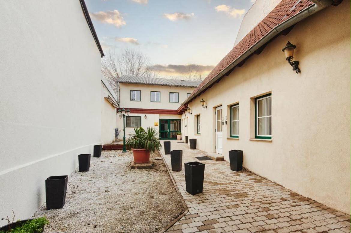 Heller Innenhof mit gepflastertem Weg, Zierpflanzen und Zugang zu den Gebäuden bei Tageslicht.