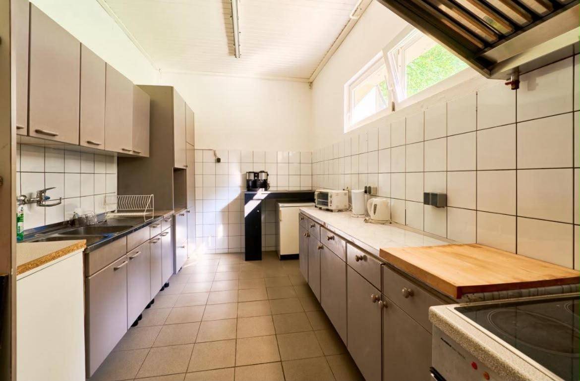 Funktionale Küche mit Fliesenboden, weißen Wänden und einfachen Schränken.
