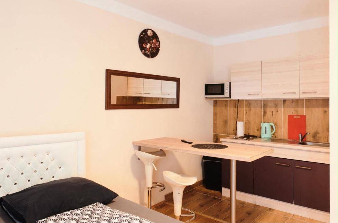 Modernes Studio-Apartment mit Küchenzeile, Doppelbett und Essbereich auf Fliesenboden.
