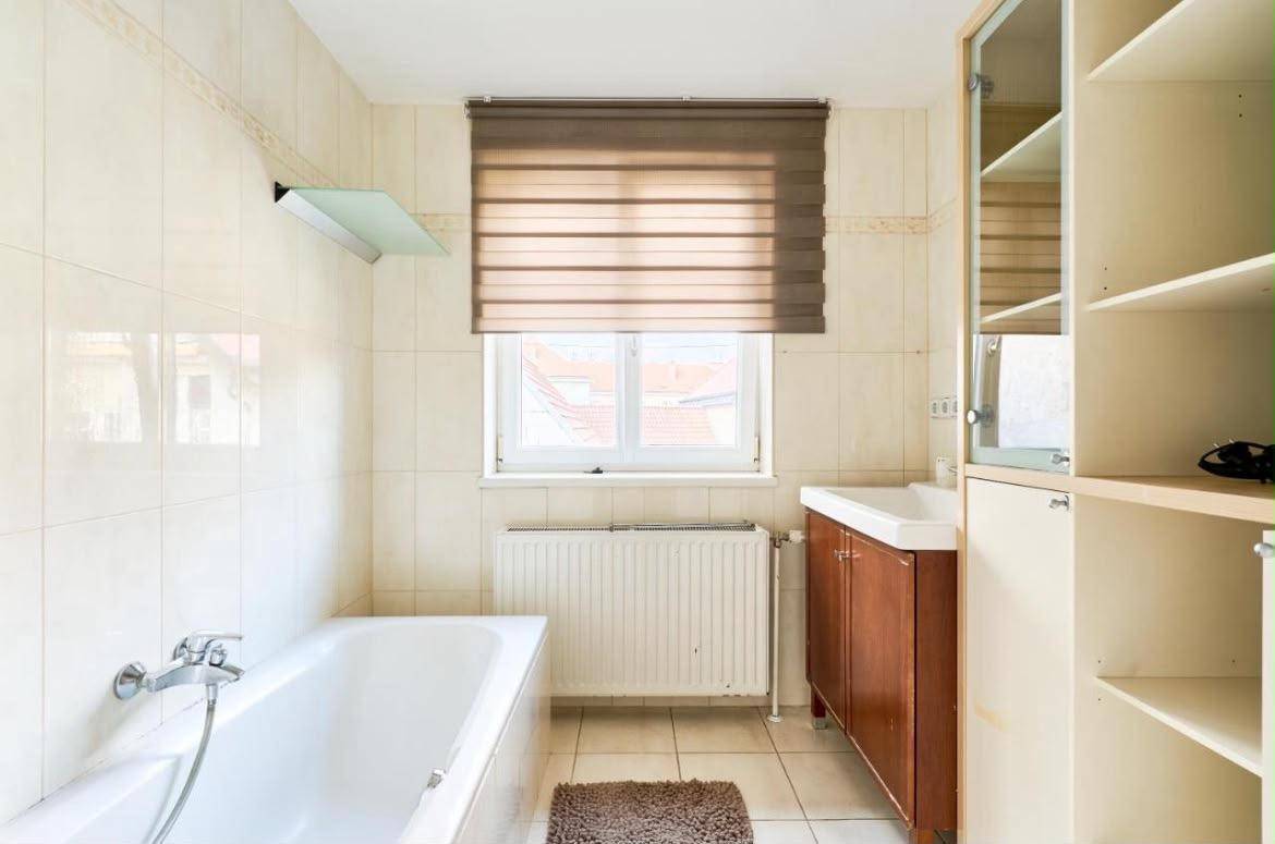 Helles Badezimmer mit Badewanne, Waschbecken und Fenster, ausgestattet mit Fliesen.