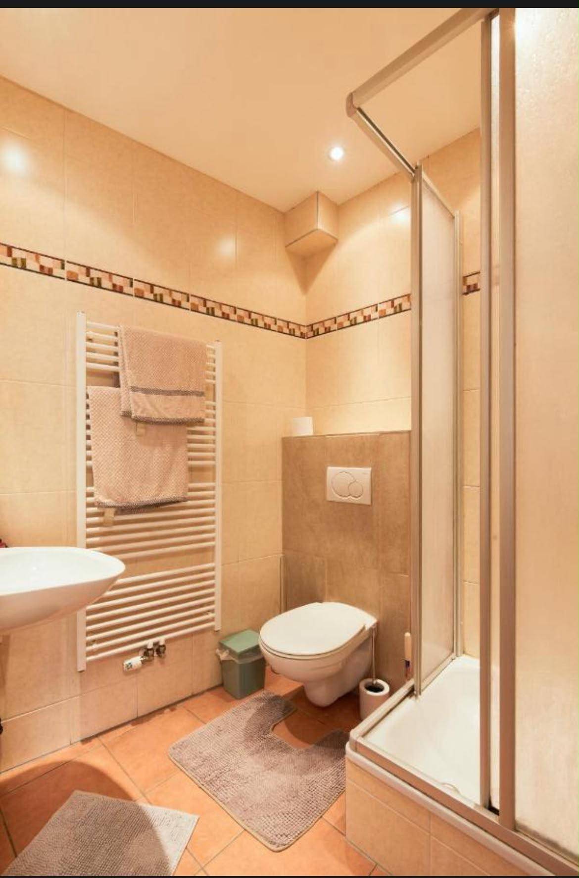 Gefliestes Badezimmer mit Dusche, WC, Waschbecken und beheiztem Handtuchhalter.