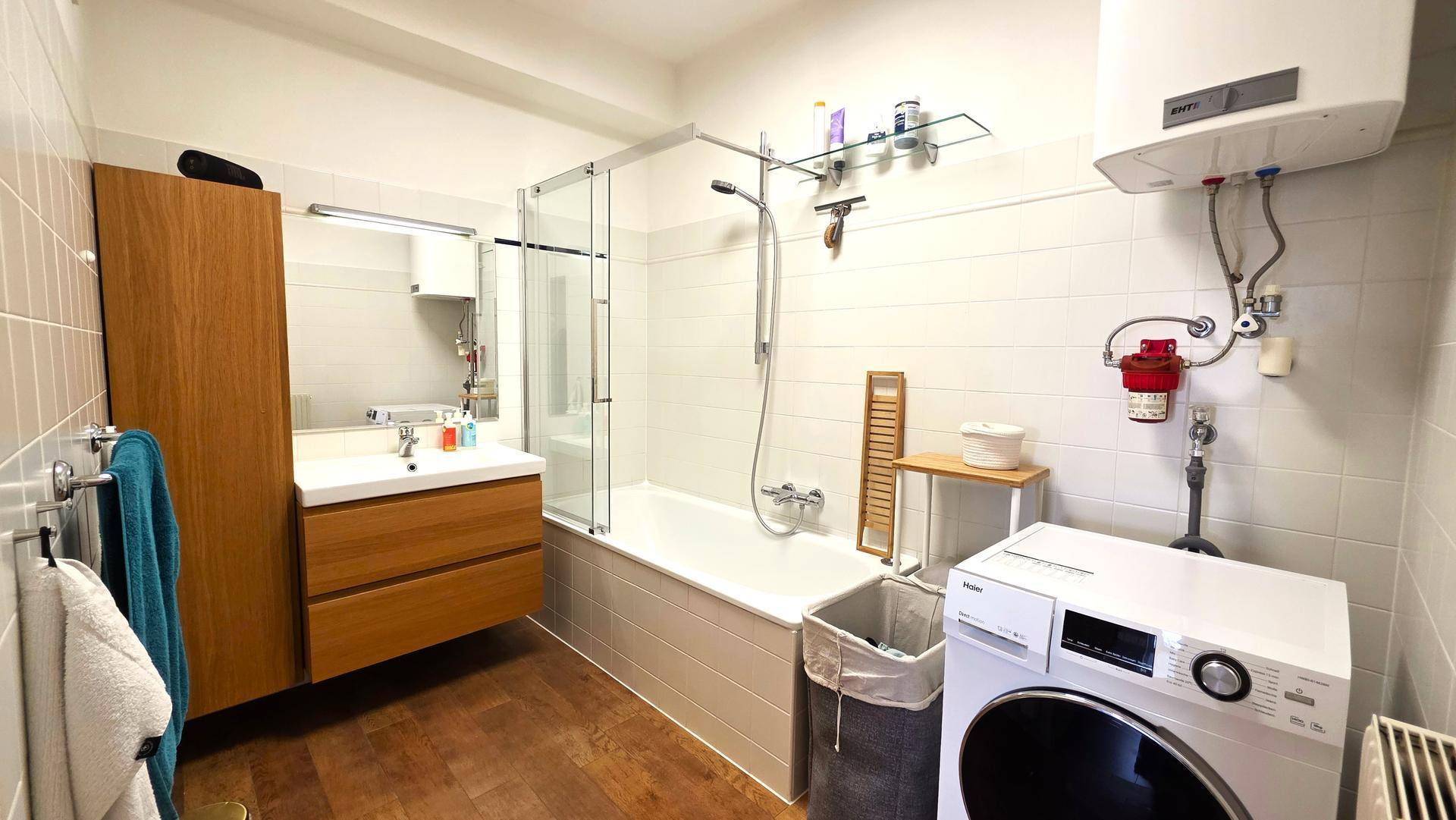 Modernes Badezimmer mit Badewanne, Dusche, Waschbecken und Waschmaschine, hell gefliest.