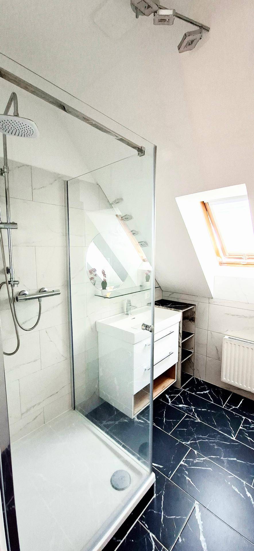Modernes Badezimmer mit begehbarer Dusche, Waschbecken und Dachfenstern, dunkler Boden.