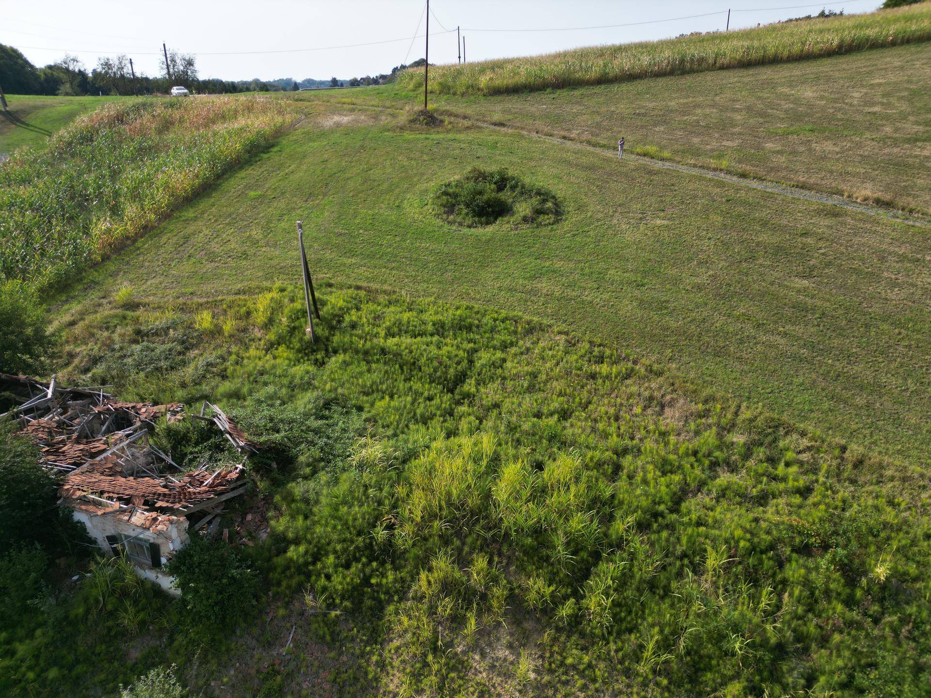 Luftaufnahme eines verfallenen Gebäudes, umgeben von Vegetation, neben einem großen grünen Feld.