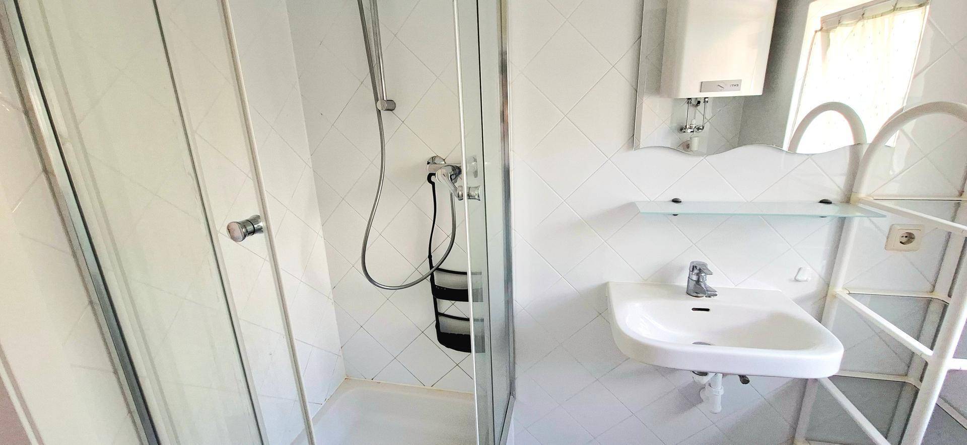 Helles Badezimmer mit Duschkabine, Waschbecken und Spiegel, gefliest in Weiß.