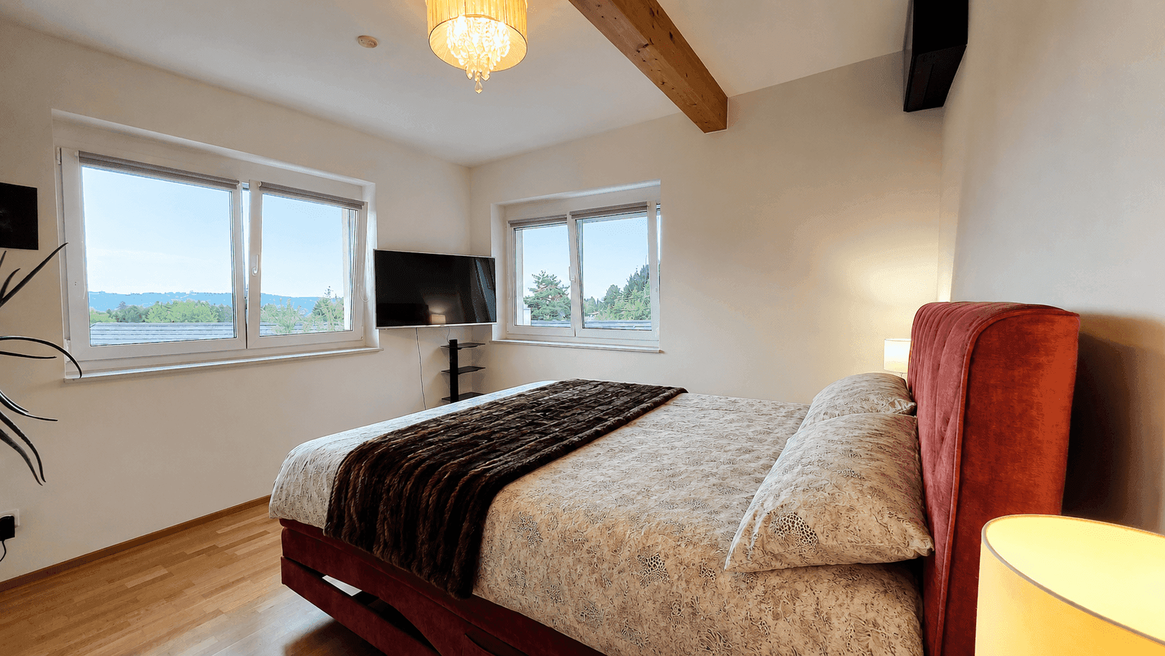 Gemütliches Schlafzimmer mit großen Fenstern, Holzbalken und Blick ins Grüne.