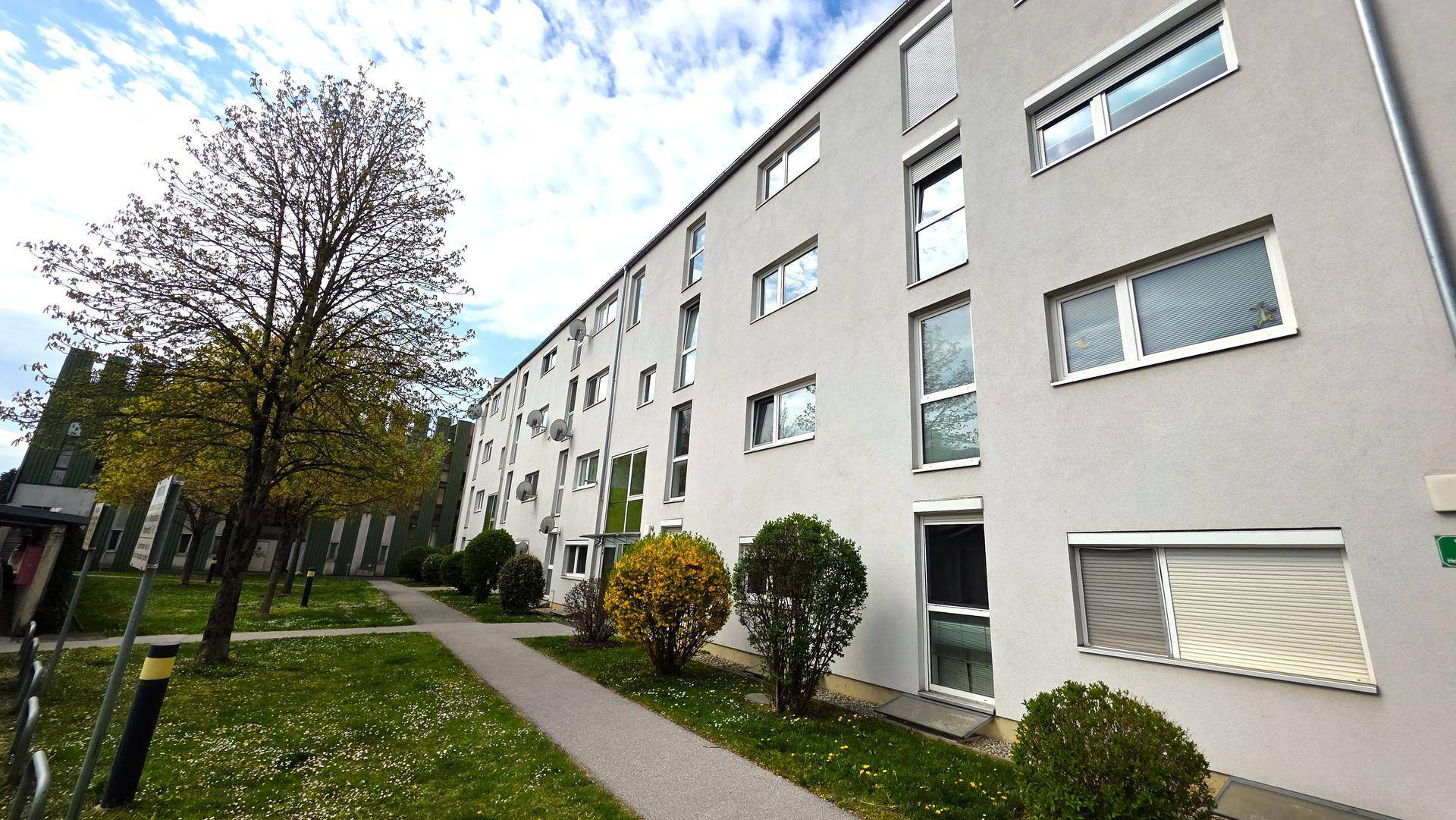 Mehrfamilienhaus mit moderner Fassade, vielen Fenstern und gepflegten Grünflächen.