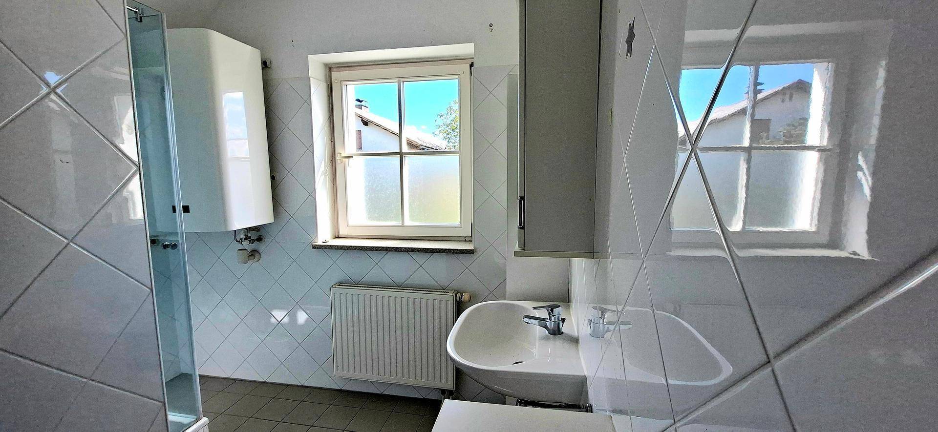 Badezimmer mit Duschkabine, Waschbecken und Fenster, gefliest in hellem Design.