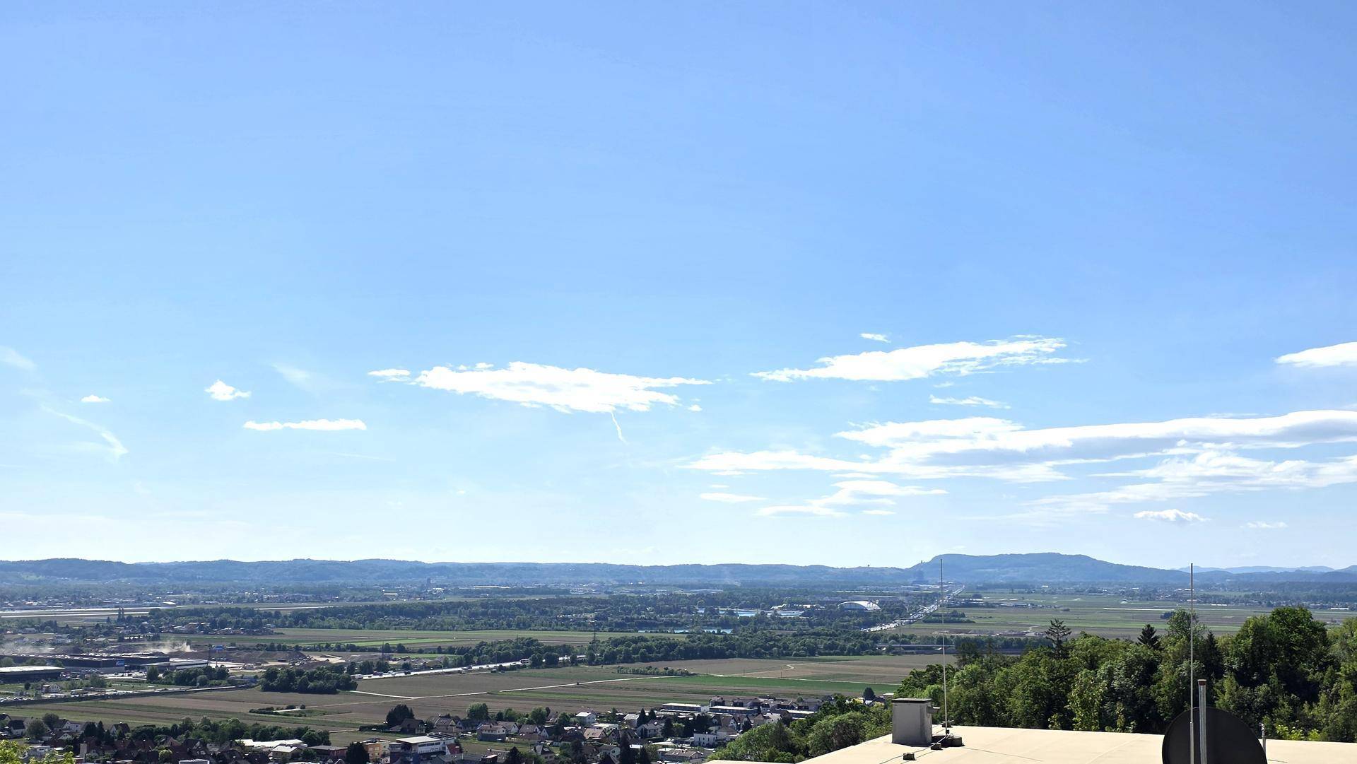 Weitläufiger Panoramablick über die Landschaft mit Feldern und fernen Bergen unter blauem Himmel.