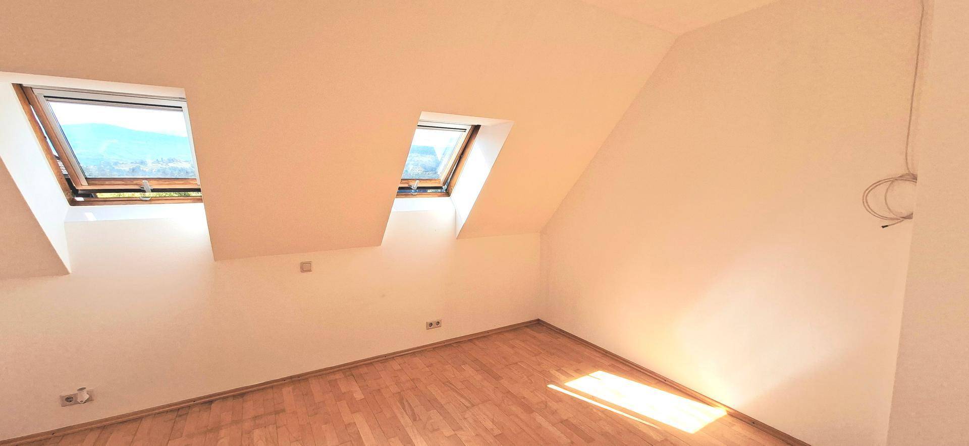 Heller Dachbodenraum mit Holzboden und zwei Dachfenstern, ideal als Schlafzimmer.