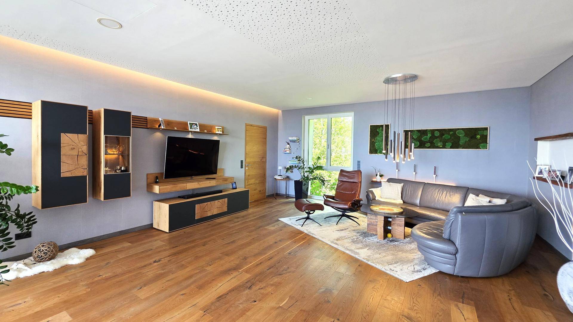 Geräumiges Wohnzimmer mit Holzboden, moderner Einrichtung und indirekter Beleuchtung.