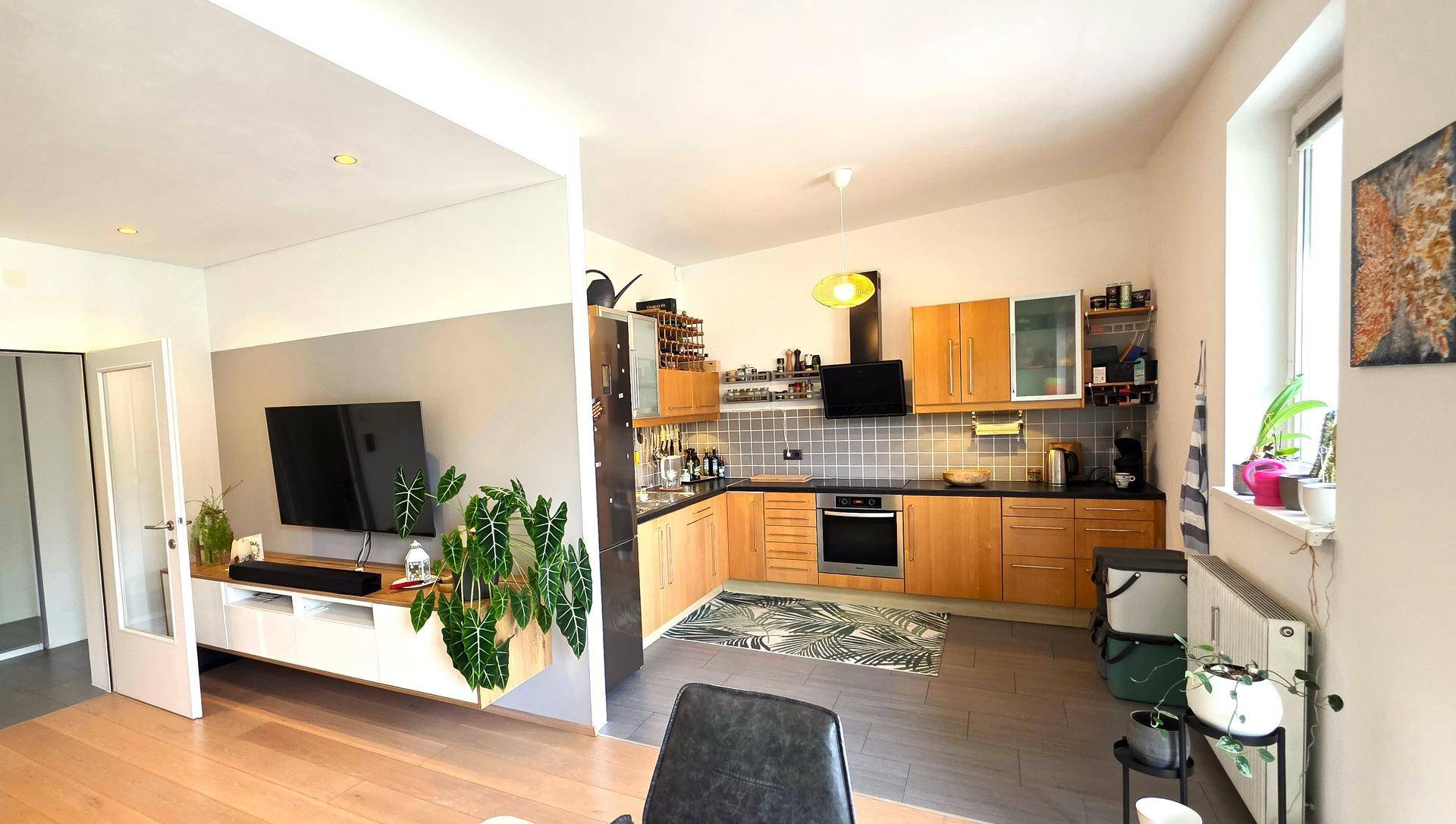 Offene Küche mit Holzschränken, modernen Geräten und Fliesenboden, angrenzend an den Wohnbereich.