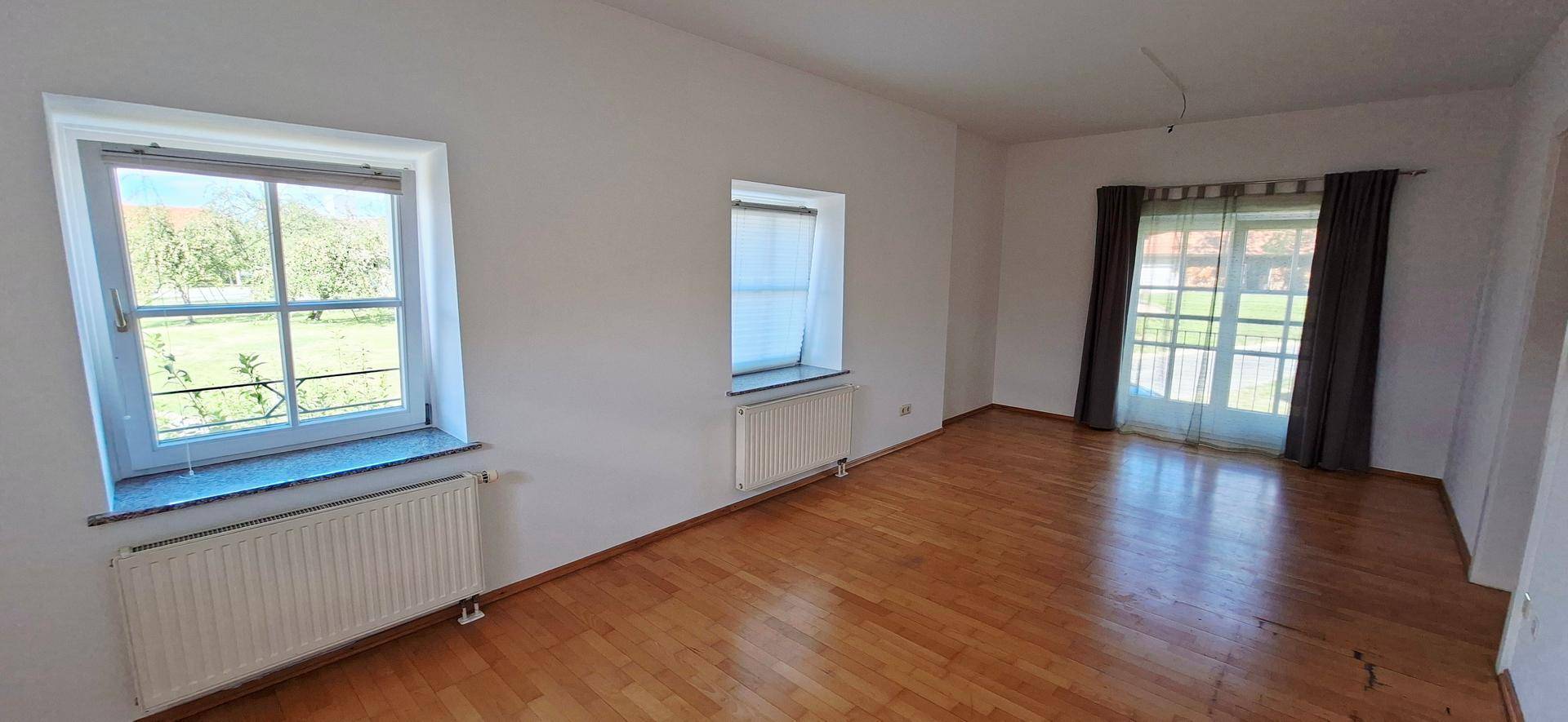Geräumiges Wohnzimmer mit Holzboden, großen Fenstern und Zugang zum Außenbereich.