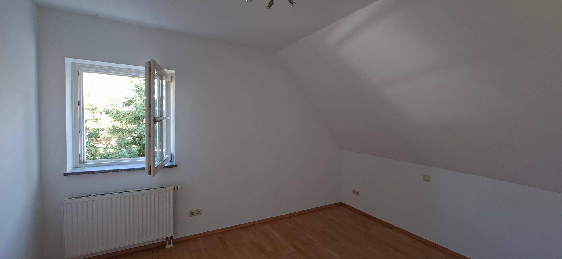 Helles Schlafzimmer im Dachgeschoss mit Holzboden und einem Fenster mit Ausblick.